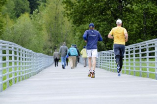 Two joggers cross a bridge as people walk ahead after gathering for a trail dedication ceremony at Marymoor Park in Redmond on Thursday.
