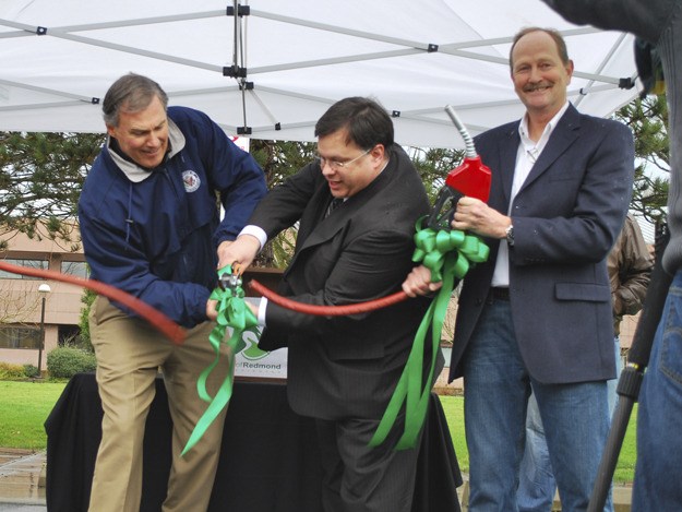 U.S. Rep. Jay Inslee (left) and Redmond Mayor John Marchione cut the ceremonial gas hose as Jim Blaisedell of Charge Northwest holds the gas pump. The event kicked off the opening four electric vehicle charging stations in Redmond