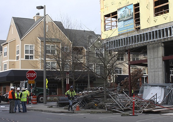 A Compass General Construction worker walks past the stack of scaffolding that fell from the yellow building onto 160th Avenue Northeast during last night's storm. The scaffolding struck a canopy at the LionsGate apartments (pictured behind and to the right) while people dined at Sages Restaurant (left). There were no injuries.