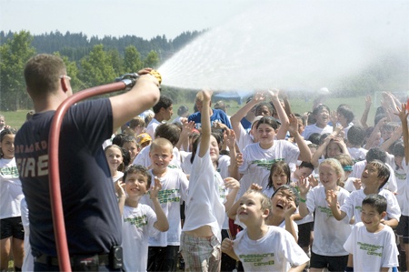 Redmond firefighter Paul “Kiwi” Atkinson hoses down kids at the Overlake Christian Church’s Ambassadors in Sport soccer camp at Sixty Acres Park in Redmond during Wednesday’s 100-degree temperatures. The high on Wednesday was 103 degrees. Temperatures are supposed to cool off into the mid-to-high 80s this weekend.