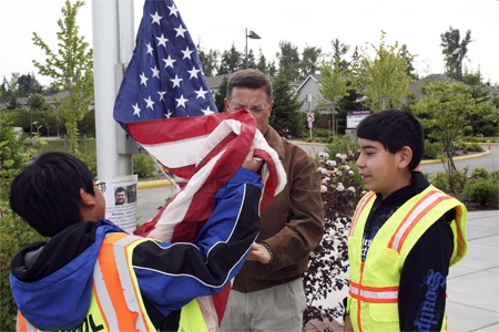 Rosa Parks Elementary students Allen Mui (left) and Alberto Gonzalez (right) get a hand from fourth grade teacher Jim Anderson as they raise the school’s flag to half-staff in honor of Samuel D. Stone (seen in poster on flagpole)