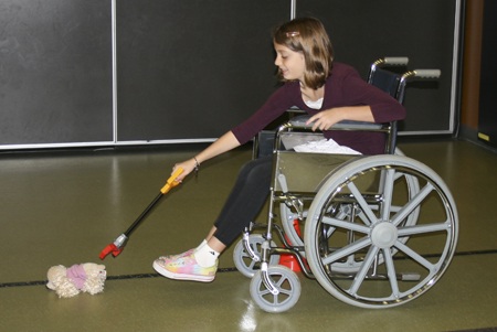Fifth-grader Tuesday Becker takes her turn at using a wheelchair and using a reaching device to retrieve an object from the floor