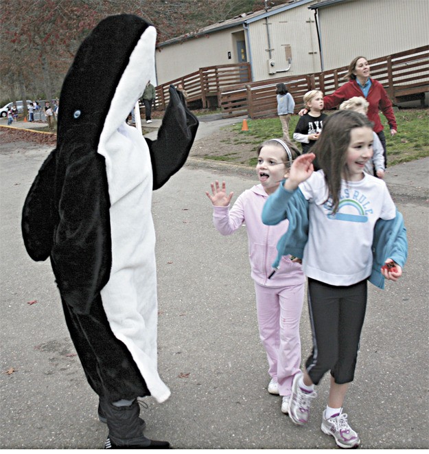 First-graders Lauren Dye (in pink) and Allie Upton wave a quick hello to the school's orca mascot (parent volunteer Fernanda Pelka) at Running Club before continuing on their way. Students run laps around the school's playground area