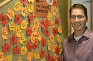 Dr. Bryan Roos stands next to the Harvest Great Patient Competition board at his office. Last month
