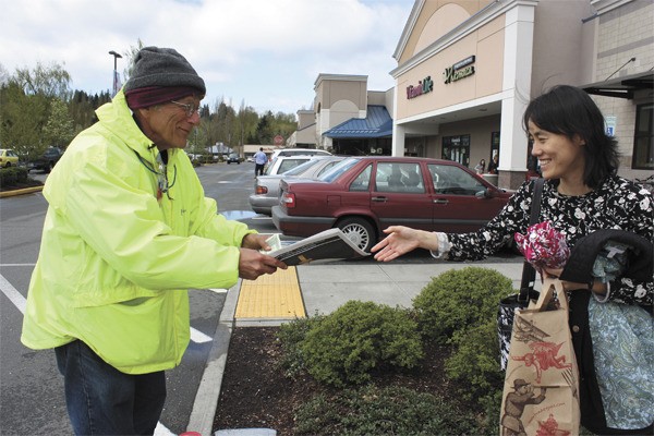 Kenneth Gutman (left) sells a Real Change newspaper to a customer outside of the Trader Joe’s in downtown Redmond.