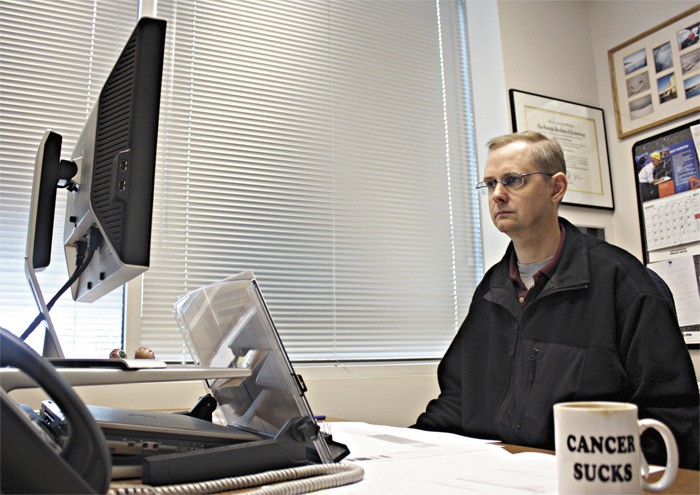 Brain cancer survivor Sam Staatz works at his desk at AECOM in Redmond. He was diagnosed in August 1999 after having a ruptured aneurysm while driving.