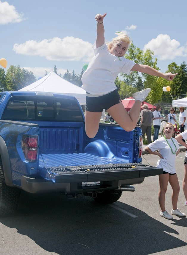Redmond High School (RHS) cheerleader Adrienne Baker jumps for joy off the tailgate of a new Ford truck as fellow cheerleader Jessie Follett