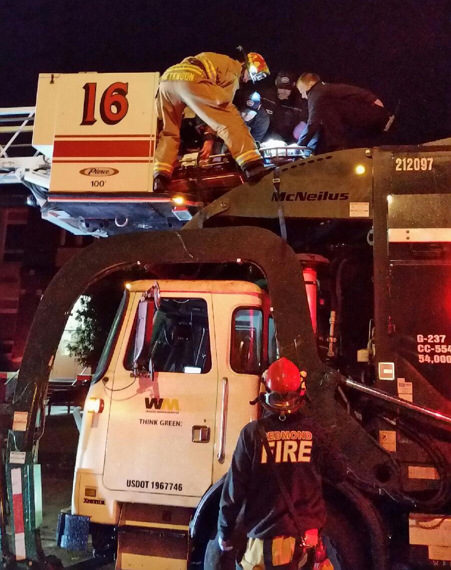 Redmond firefighters work to rescue a man from a Waste Management truck after he was dumped from a dumpster in downtown. Courtesy of Redmond Police Department