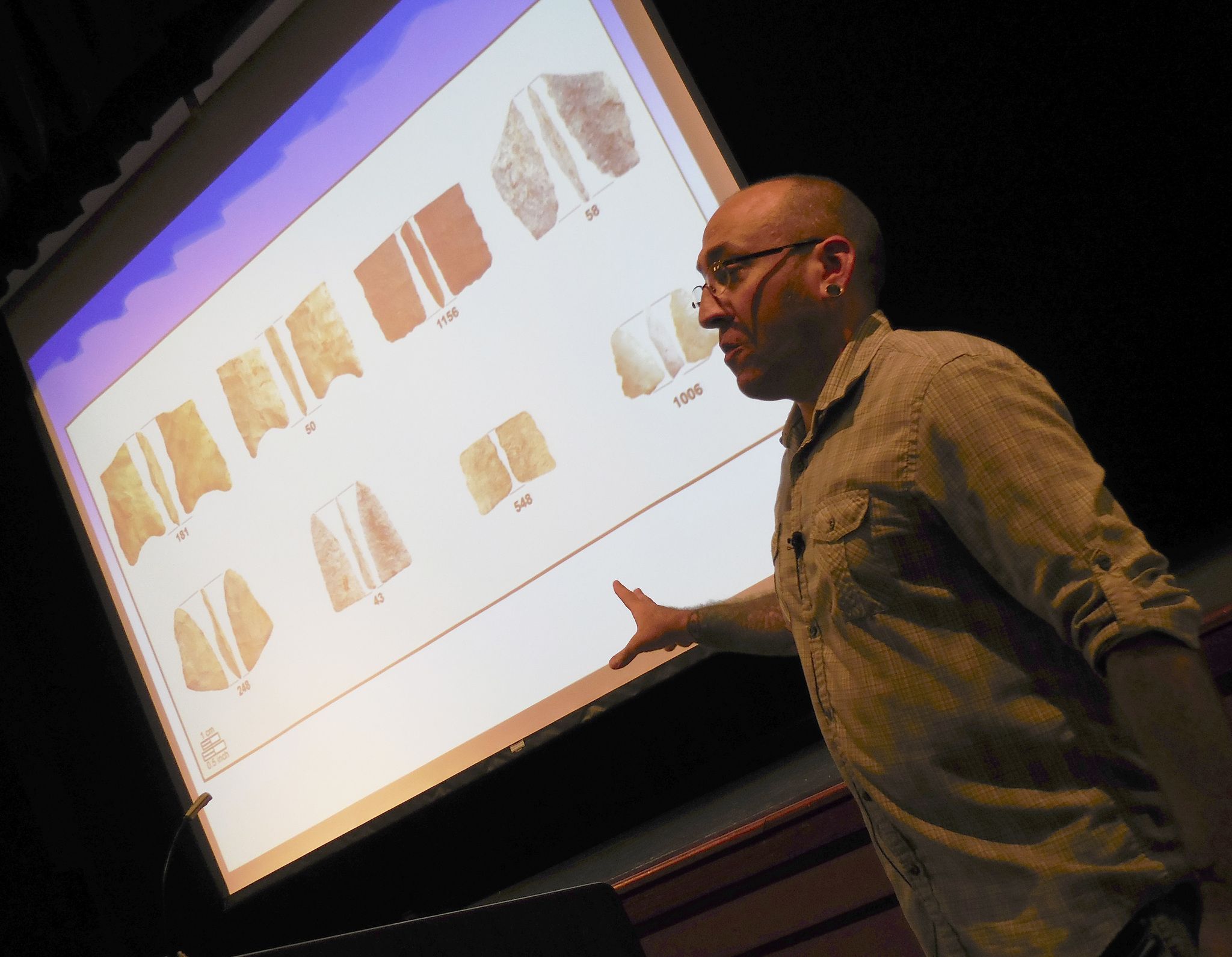 With a photo of parts of 10,000-year-old stone tools on the screen behind him, Dr. Robert Kopperl discusses the major find in Redmond at a 2015 meeting. Reporter file photo