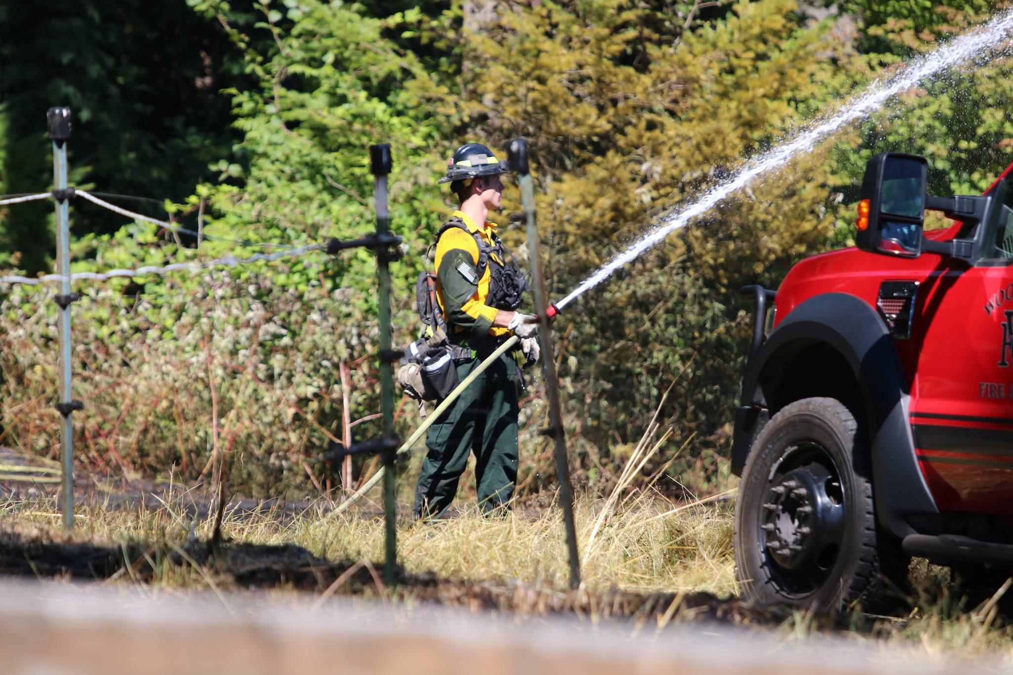 A firefighter sprays down remaining hot spots after units from three departments worked to knock down a brush fire on the border of Redmond, Duvall and Woodinville on Tuesday afternoon. Aaron Kunkler/Redmond Reporter