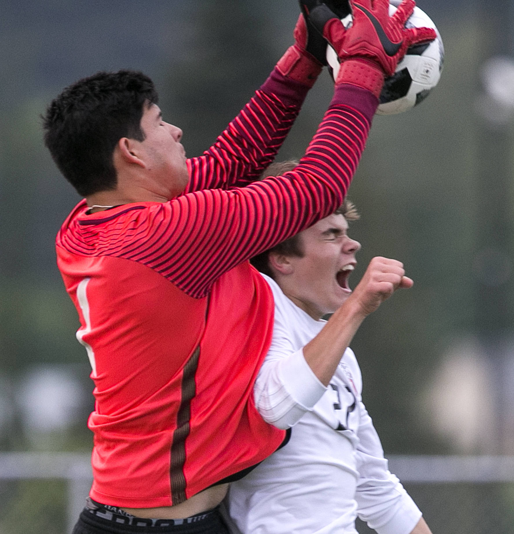 Redmond’s Ricardo Escalante makes a save over Snohomish’s Eli Esterly in the quarterfinals Friday night at Veterans Memorial Stadiums in Snohomish on May 18. (Kevin Clark / The Herald)