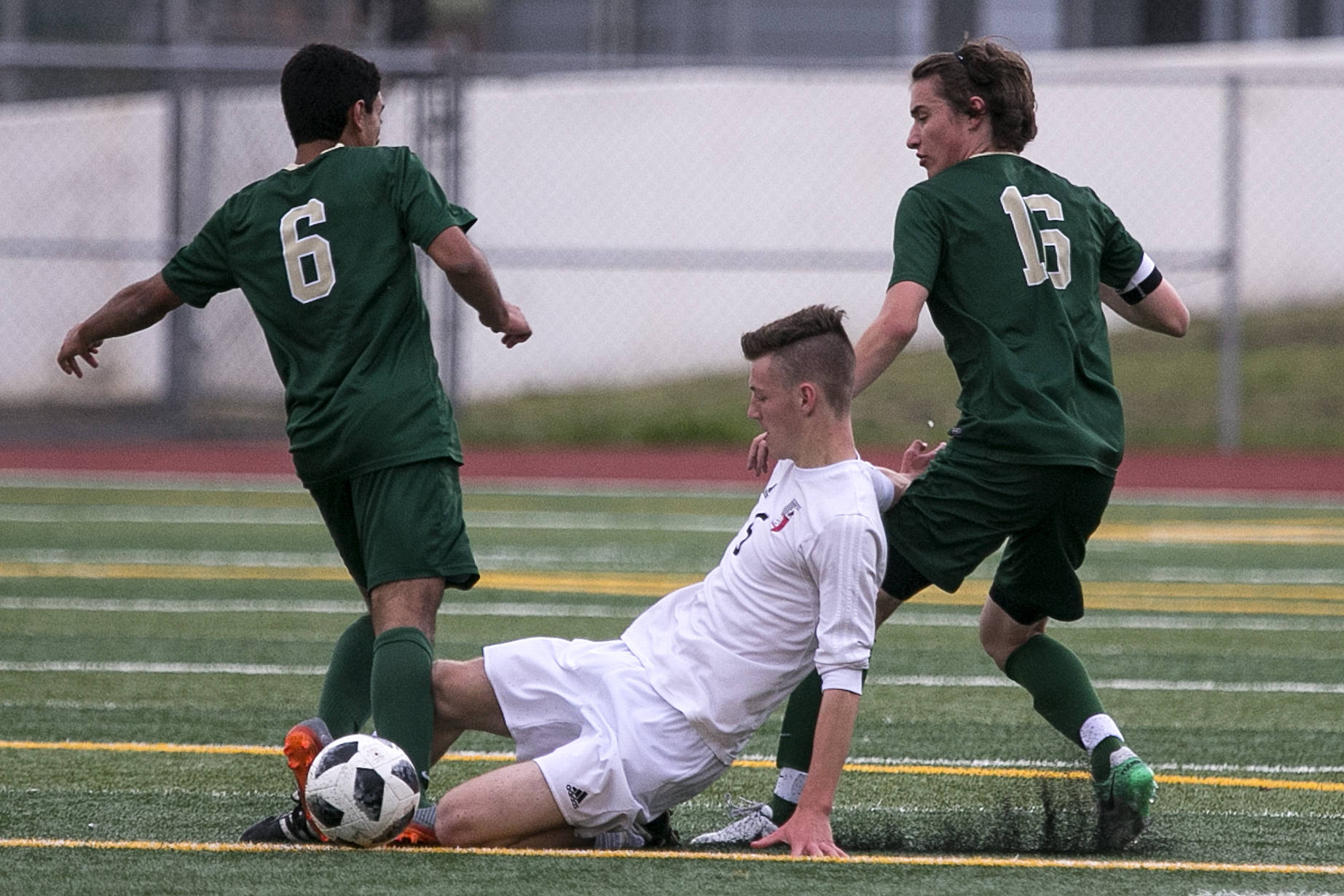 Snohomish’s Liam Raney slides to dislodge the ball from Redmond’s Victor Araujo (left) with Jacen Stein trailing in the quarterfinals Friday night at Veterans Memorial Stadiums in Snohomish on May 18. (Kevin Clark / The Herald)