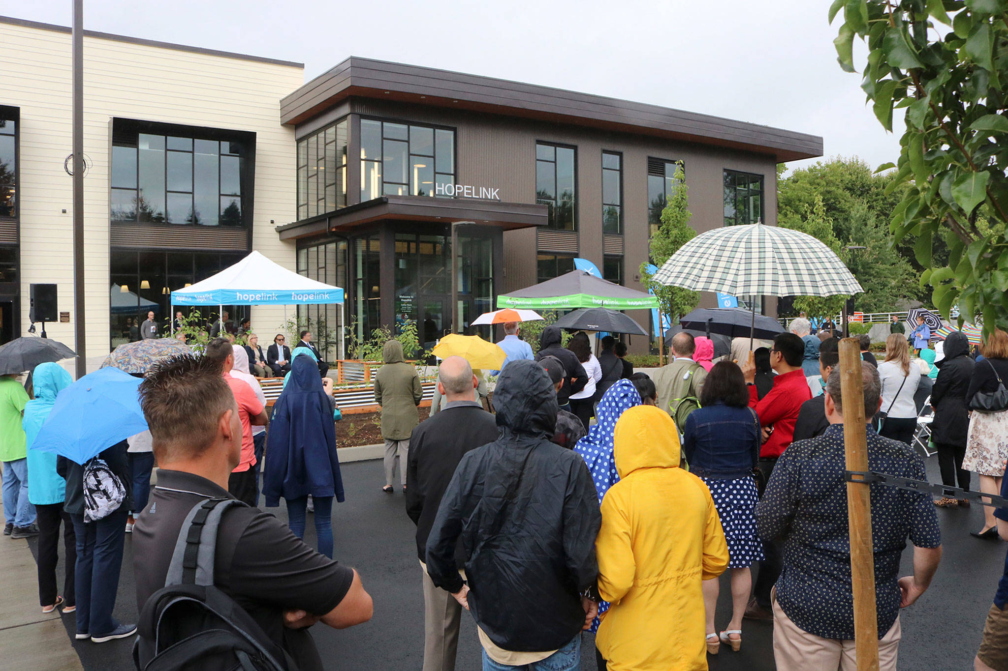Attendees at Hopelink Redmond’s grand opening on Aug. 3 wear rain jackets and hold umbrellas while listening to the featured speakers at the event. Katie Metzger/staff photo