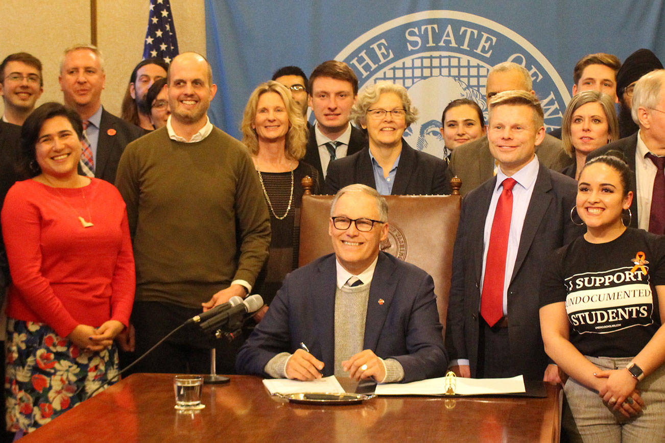 Gov. Jay Inslee signs the first bill of the 2020 legislative session into law. On the right stands the bill’s primary sponsor, Sen. Jamie Pedersen, D-Seattle, who is wearing a red tie. Photo by Cameron Sheppard, WNPA News Service