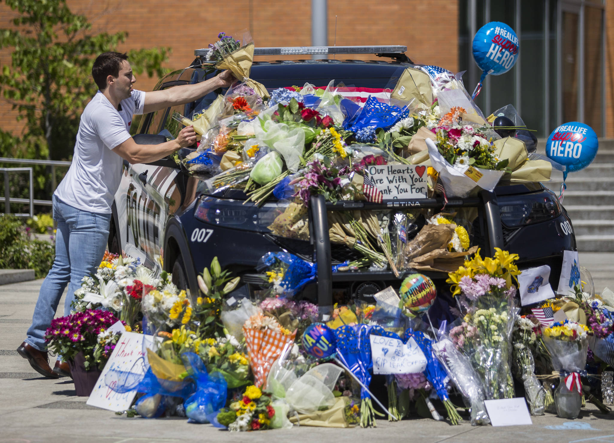 Tony Mandeville places a bouquet of flowers on the windshield of a Bothell Police Department vehicle that was turned into a memorial Tuesday in front of Bothell City Hall. (Olivia Vanni / The Herald)