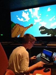 Daniel Hert plays “Minecraft” on his laptop with another scene on the big screen.