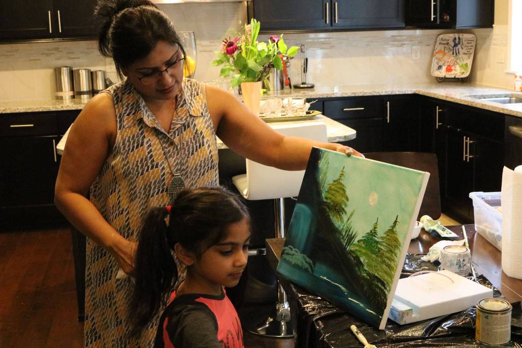 Haritha Kamakoti holds up the canvas as her daughter, Ira Ganjikunta, 6, puts the finishing touches on a painting at their Redmond home. CATHERINE KRUMMEY/Kirkland Reporter