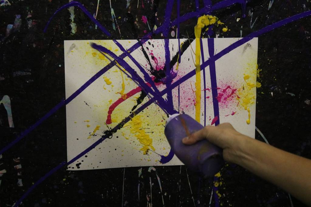 Art Works owner Chelsea Sherman dashes paint against a canvas in a splash room in the studio. Aaron Kunkler/Redmond Reporter