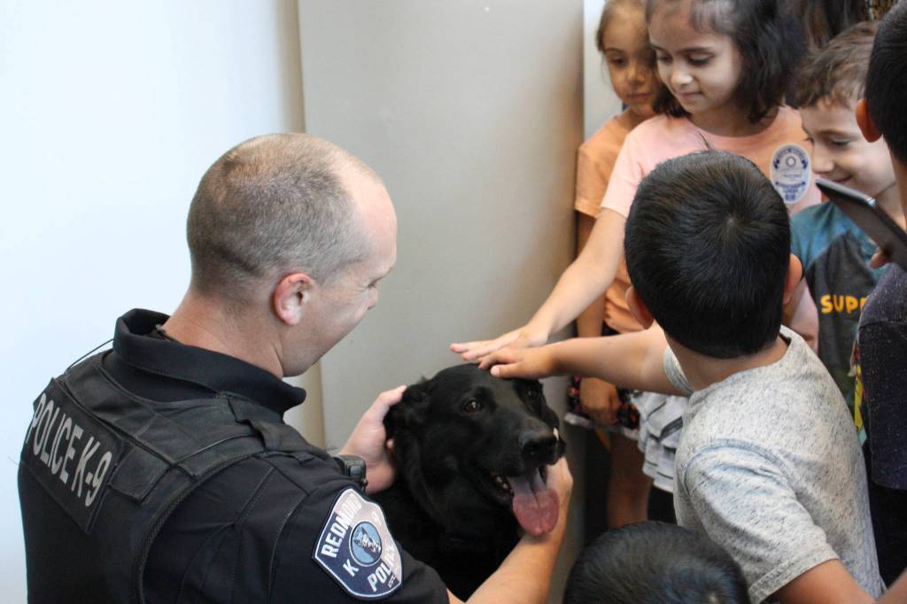 Officer Dan Smith and his partner Remy meet with local children at the Little Free Library opening. Remy seemed overwhelmed by the wave of head pats and back scratches. Kailan Manandic, Redmond Reporter