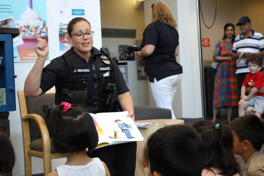 Sergeant Julie Beard reads Officer Buckle and Gloria, promoting safety to local children, while sitting next to the Little Free Library. Kailan Manandic, Redmond Reporter