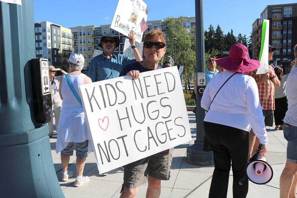 A demonstrator holds sign that reads, Kids Need Hugs Not Cages on July 12 at Redmonds Downtown Park.