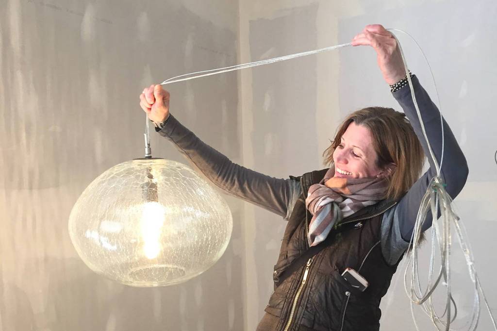 Artist Julie Conway of Illuminata Glass holds one of her light fixture creations in Hashtag Cannabis Seattle storefront, currently being remodeled. Some of her works will be a part of the new Redmond store as well, part of the companys support of local artists and businesses, especially those operated by women. Photo by Kim Bevington