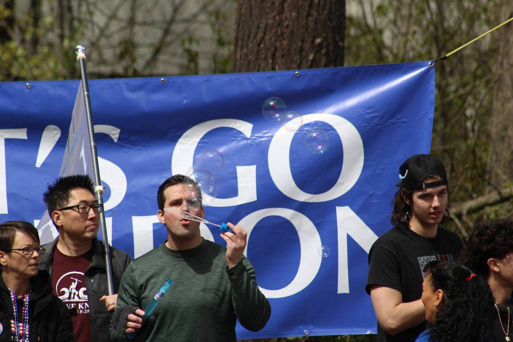 A member of the crowd blows bubbles in front of a giant LETS GO BRANDON sign as the crowd awaits the arrival of President Biden. Photo by Alex Bruell/Sound Publishing